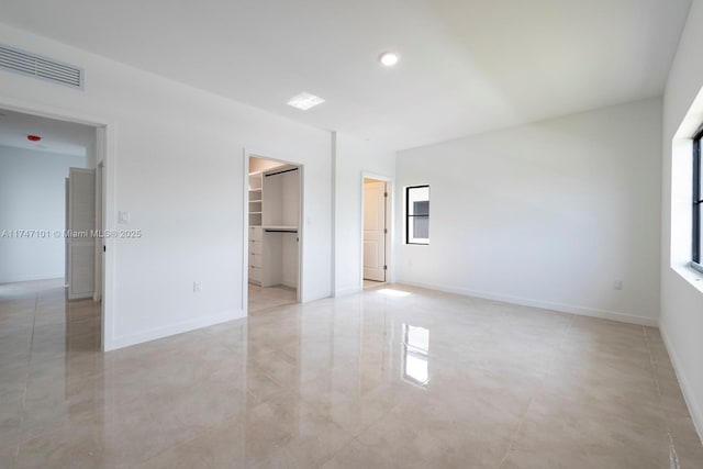 unfurnished bedroom with a closet, visible vents, a walk in closet, and baseboards