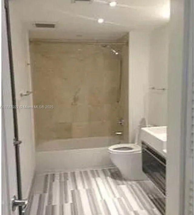 bathroom with hardwood / wood-style flooring, tiled shower / bath, and toilet