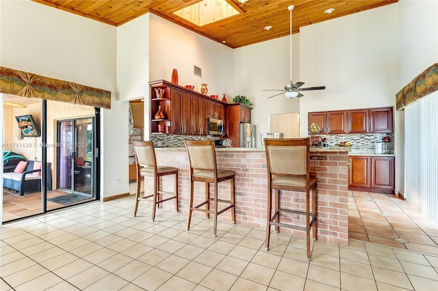 653 NW 110th Ave, Coral Springs, FL 33071 - kitchen featuring stainless steel appliances, wood ceiling, backsplash, light tile patterned floors, and a kitchen breakfast bar