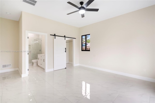 unfurnished bedroom with ceiling fan, connected bathroom, and a barn door