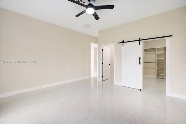 unfurnished bedroom with ceiling fan, a closet, a walk in closet, and a barn door