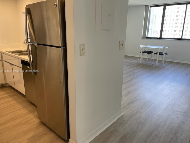 kitchen featuring dishwashing machine, electric panel, stainless steel fridge, light hardwood / wood-style floors, and sink