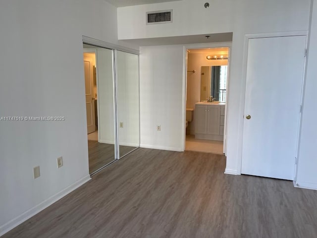 unfurnished bedroom featuring ensuite bathroom, hardwood / wood-style flooring, and a closet