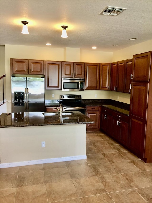 kitchen featuring sink, stainless steel appliances, a textured ceiling, and dark stone counters