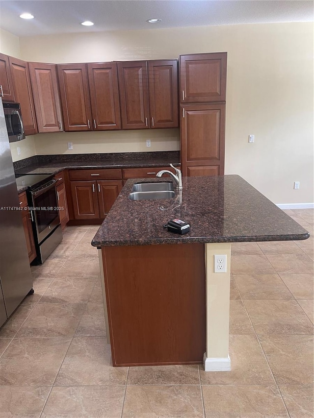 kitchen featuring dark stone countertops, an island with sink, appliances with stainless steel finishes, and sink