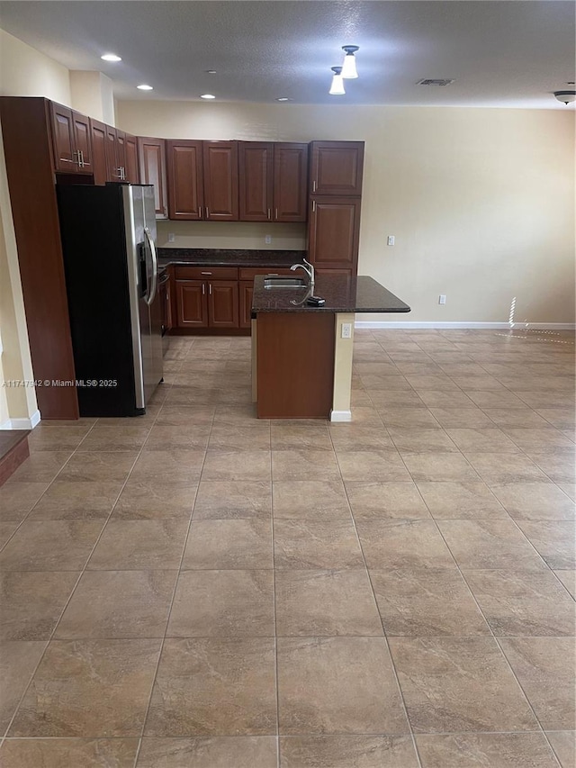 kitchen featuring an island with sink, a breakfast bar, stainless steel fridge, light tile patterned floors, and sink