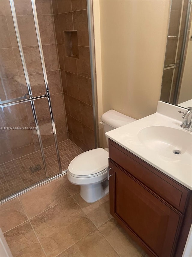 bathroom with toilet, vanity, tile patterned flooring, and a shower with shower door