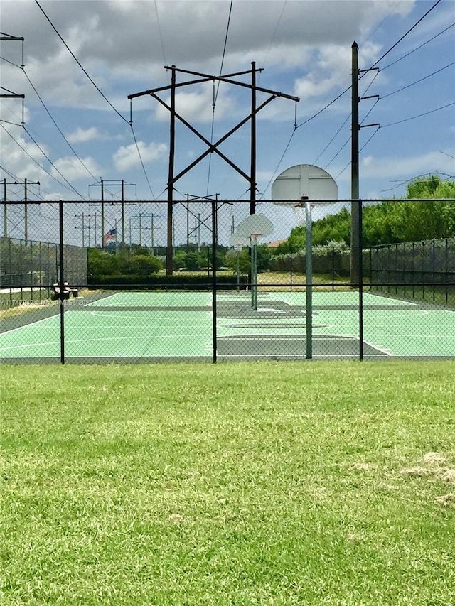 view of tennis court featuring a yard and basketball hoop