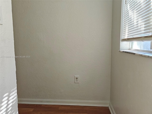 empty room with a textured wall, wood finished floors, and baseboards