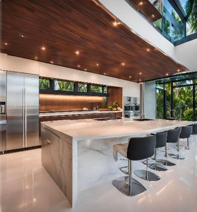 kitchen featuring a large island, modern cabinets, appliances with stainless steel finishes, wood ceiling, and light stone countertops