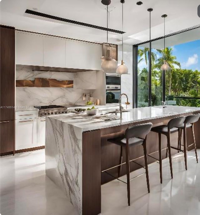 kitchen with stainless steel oven, white cabinetry, a center island with sink, and modern cabinets