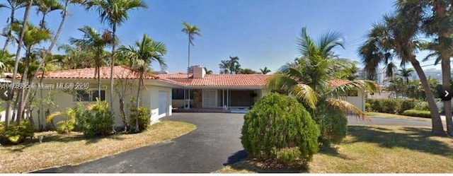 view of front of home featuring aphalt driveway, a tile roof, a chimney, stucco siding, and a front lawn