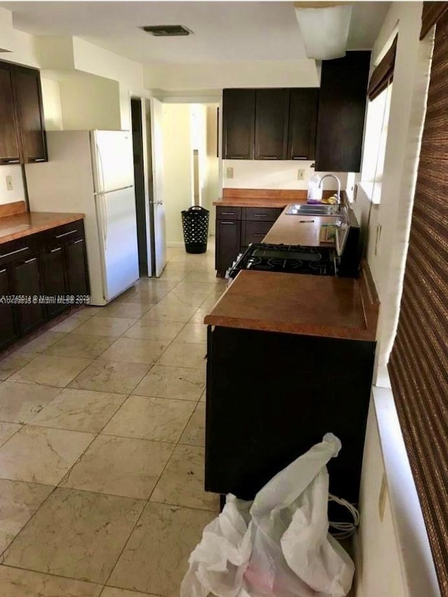 kitchen featuring light countertops, stove, freestanding refrigerator, a sink, and dark brown cabinets