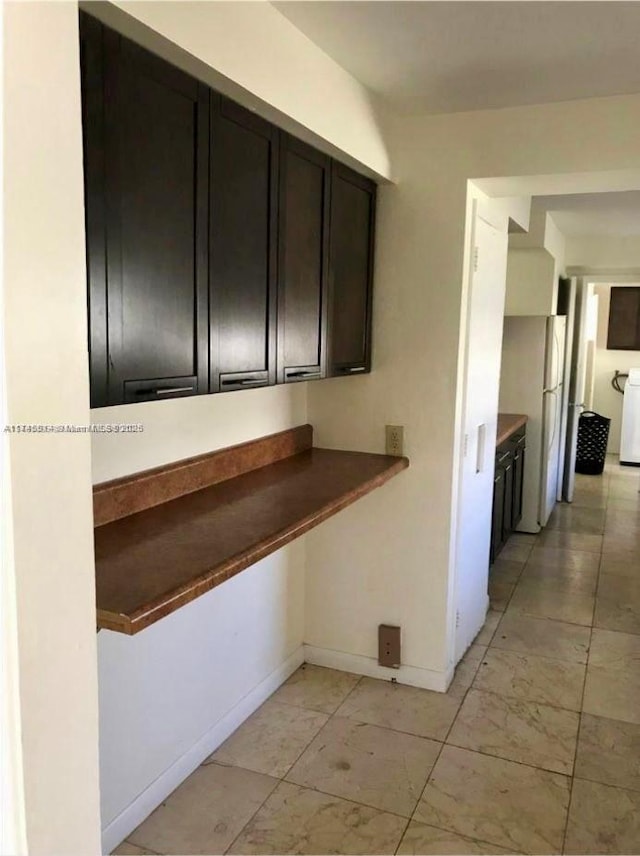 kitchen featuring freestanding refrigerator, washer / dryer, dark brown cabinetry, and baseboards