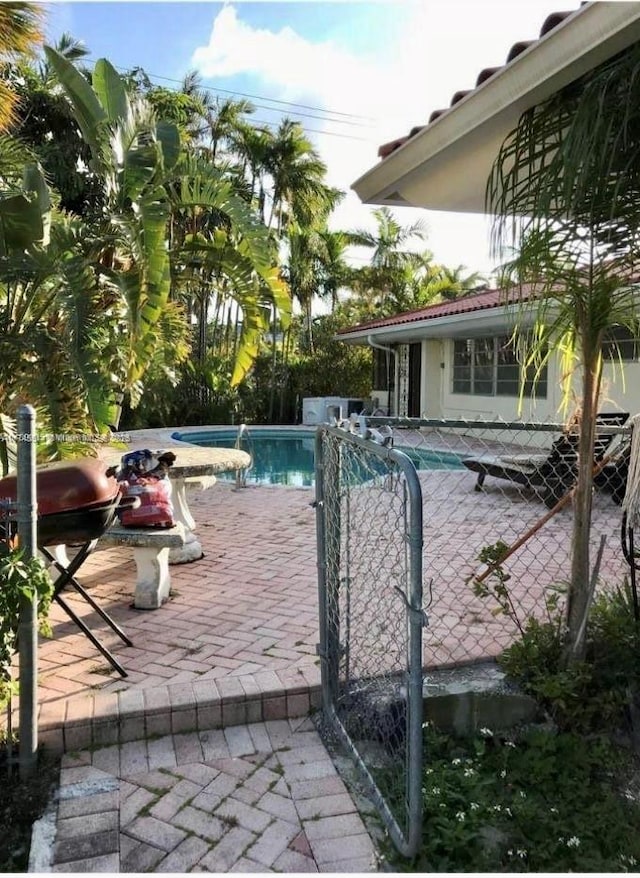 pool with a patio, fence, and a jacuzzi