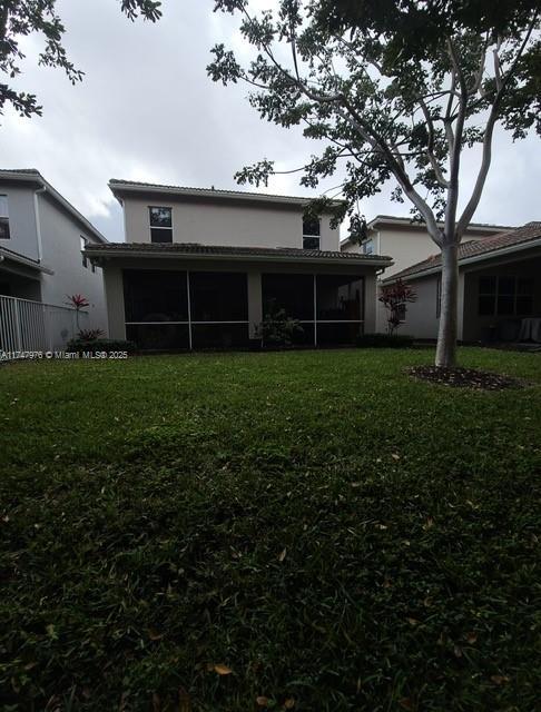 rear view of house featuring a sunroom, a yard, fence, and stucco siding