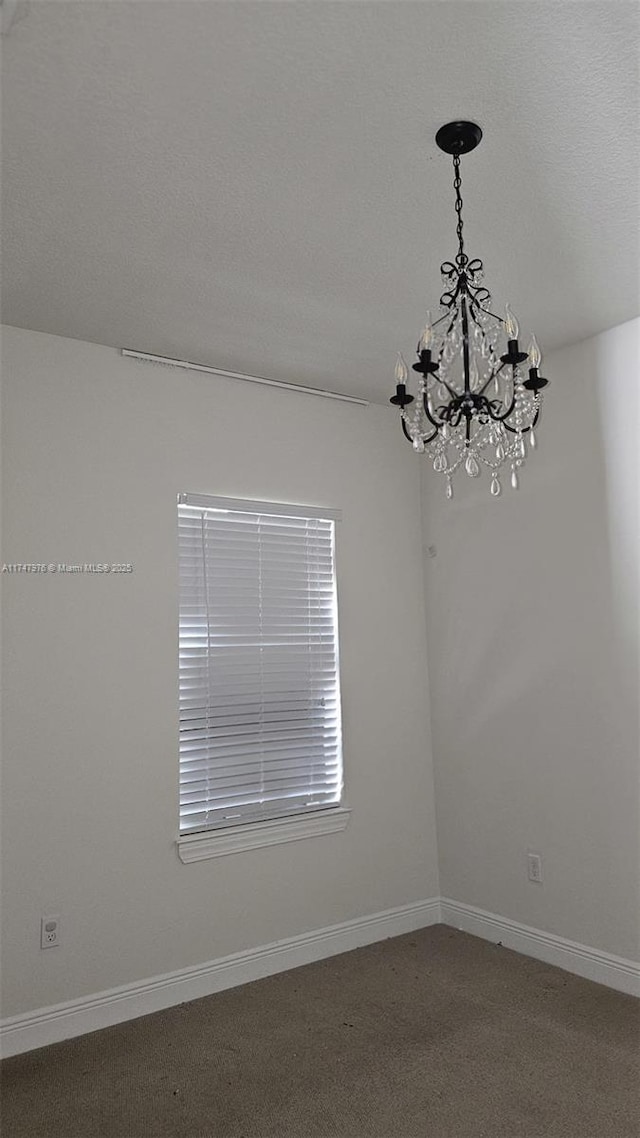 carpeted spare room featuring a notable chandelier, a textured ceiling, and baseboards