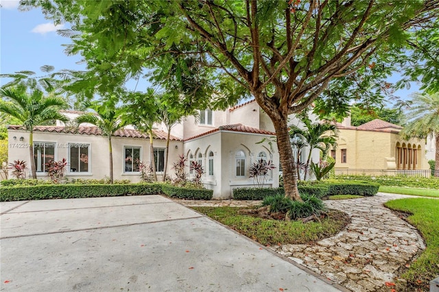 mediterranean / spanish house featuring stucco siding, a tiled roof, and fence