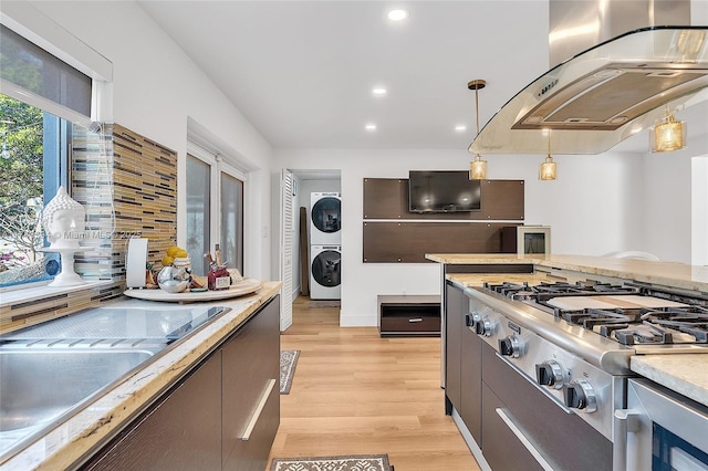 kitchen featuring stacked washer / drying machine, ventilation hood, light countertops, light wood-style floors, and pendant lighting