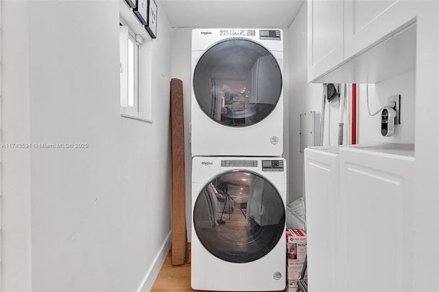 washroom featuring stacked washer / drying machine, cabinet space, light wood-style flooring, and baseboards