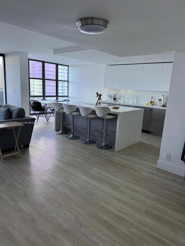 kitchen with white cabinetry, a center island, stainless steel dishwasher, hardwood / wood-style floors, and a kitchen bar