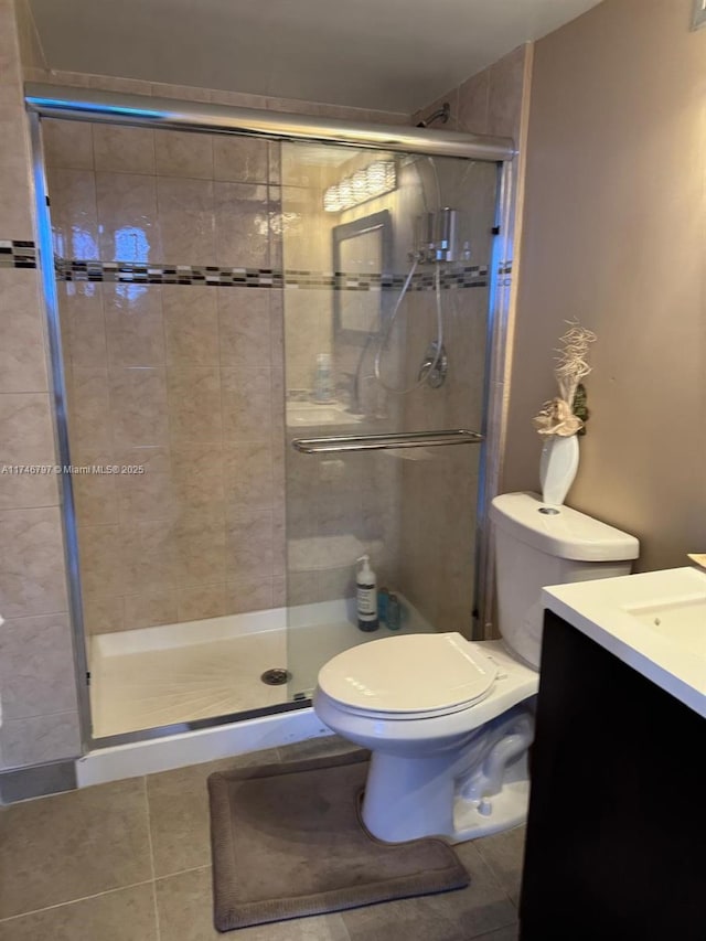 bathroom featuring tile patterned floors, toilet, vanity, and a shower with shower door