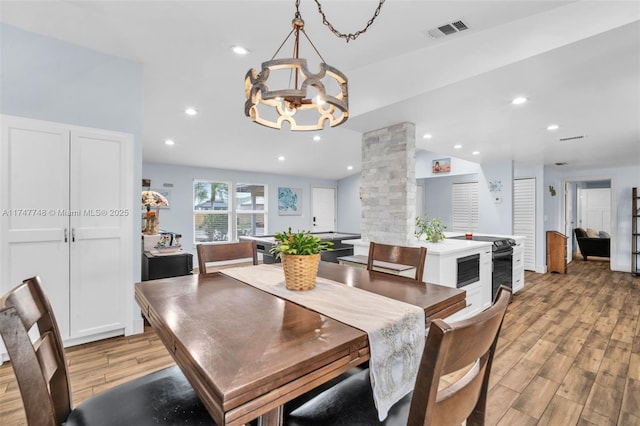 dining space featuring light hardwood / wood-style floors, vaulted ceiling, ornate columns, and an inviting chandelier