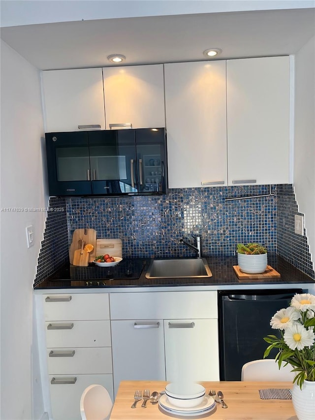 kitchen featuring dark countertops, backsplash, white cabinetry, a sink, and dishwashing machine