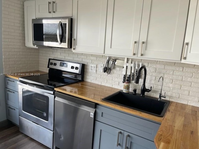 kitchen featuring butcher block counters, a sink, white cabinetry, appliances with stainless steel finishes, and backsplash