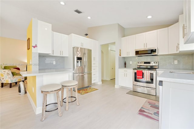 kitchen with appliances with stainless steel finishes, white cabinetry, a kitchen breakfast bar, and light hardwood / wood-style flooring