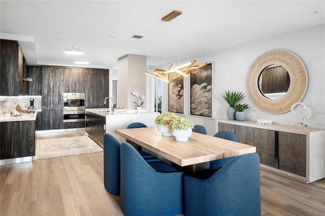 dining room with sink, a notable chandelier, and light hardwood / wood-style floors