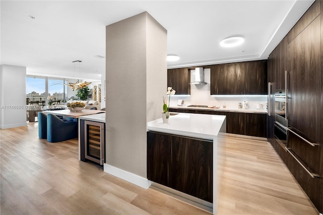 kitchen with a kitchen island, wine cooler, gas stovetop, wall chimney range hood, and pendant lighting