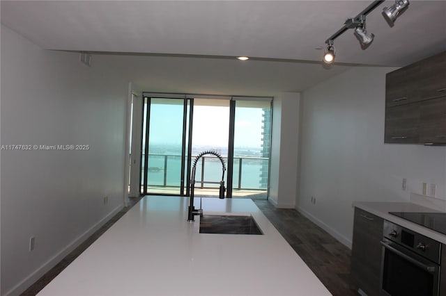 kitchen featuring floor to ceiling windows, black appliances, a water view, sink, and track lighting