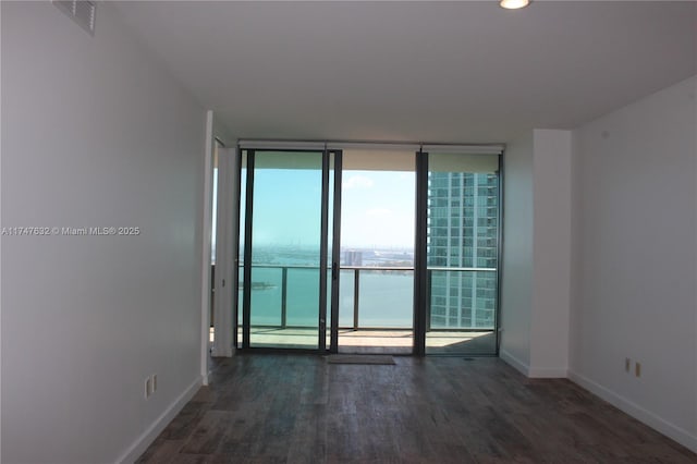 empty room with a water view, expansive windows, and dark hardwood / wood-style floors