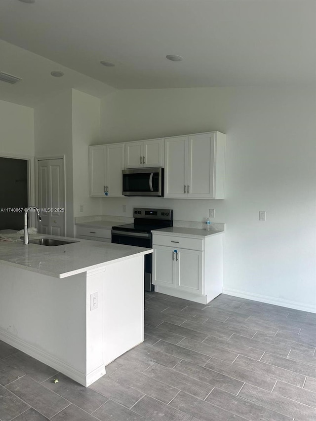 kitchen featuring appliances with stainless steel finishes, sink, vaulted ceiling, a kitchen island, and white cabinets