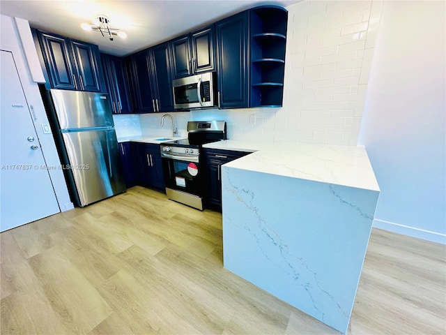 kitchen with light stone counters, light wood-style flooring, appliances with stainless steel finishes, open shelves, and tasteful backsplash