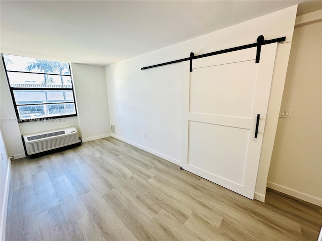 empty room featuring baseboards, a wall mounted air conditioner, light wood finished floors, and a barn door