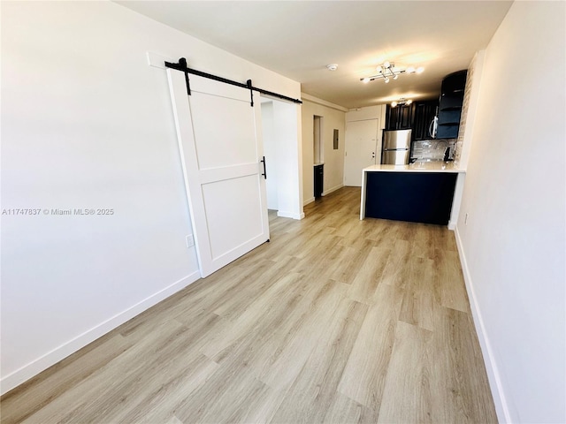 kitchen featuring a barn door, freestanding refrigerator, light countertops, dark cabinetry, and backsplash