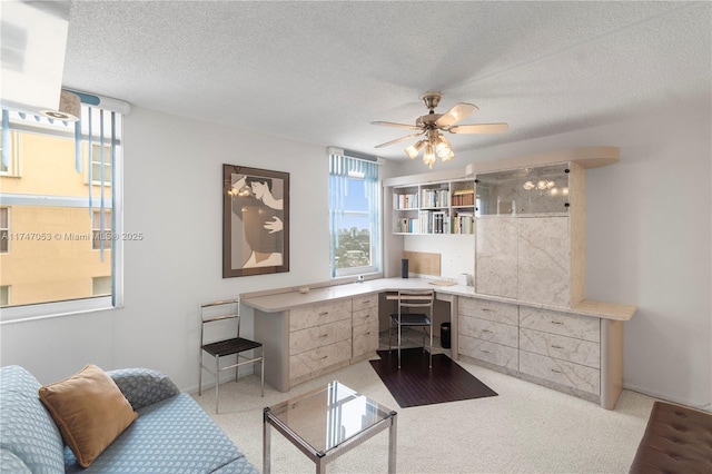 office featuring a textured ceiling, ceiling fan, built in desk, and light carpet