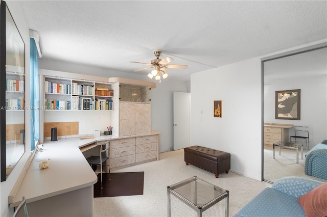 office space with a textured ceiling, built in desk, light carpet, and a ceiling fan