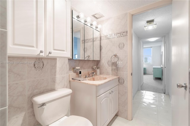 bathroom featuring a textured ceiling, toilet, visible vents, vanity, and tile walls