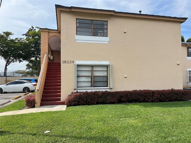 view of property exterior featuring a lawn, stairway, and stucco siding