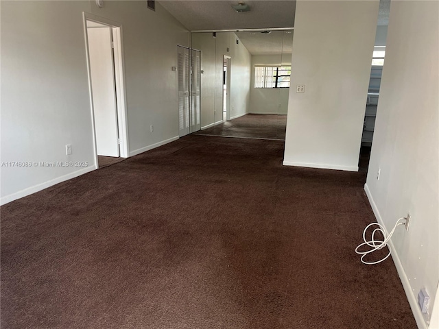 hall featuring dark colored carpet and baseboards