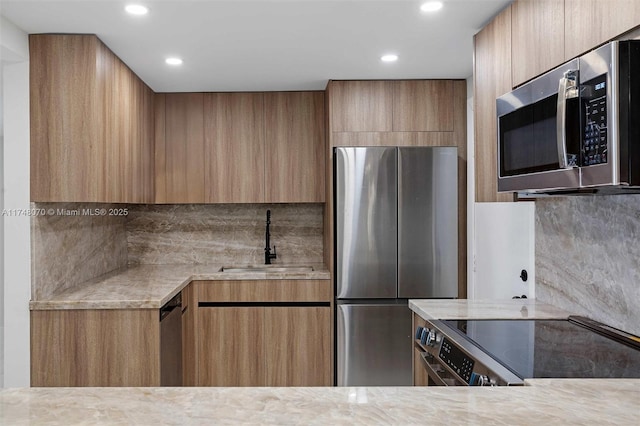 kitchen featuring sink, backsplash, appliances with stainless steel finishes, and light stone countertops