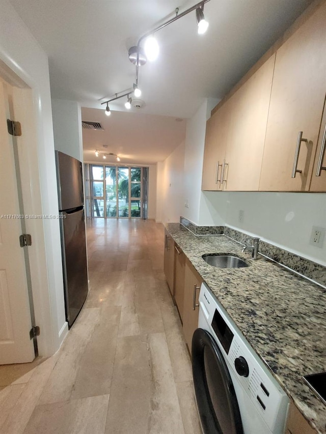 kitchen featuring stainless steel fridge, sink, stone counters, washer / dryer, and rail lighting