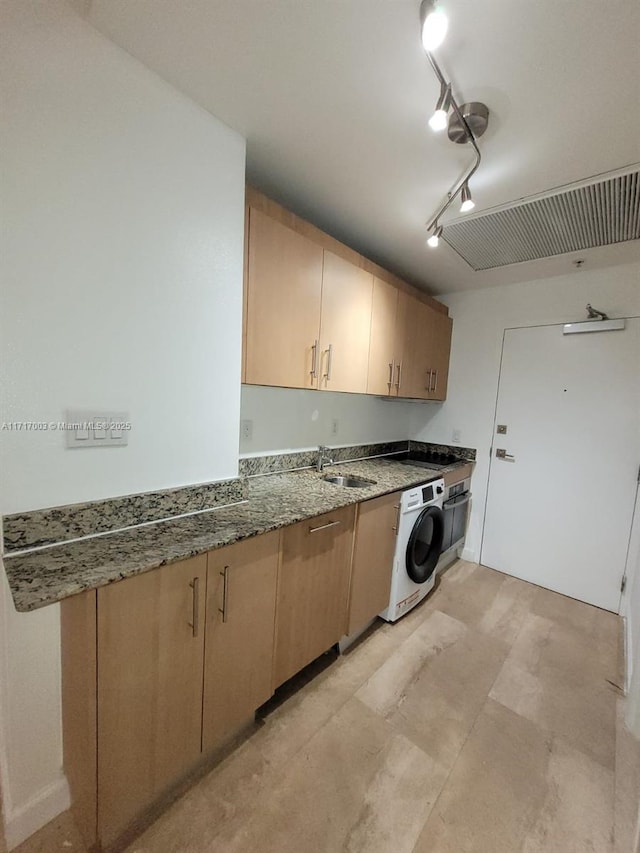 kitchen with sink, oven, track lighting, washer / dryer, and light brown cabinetry