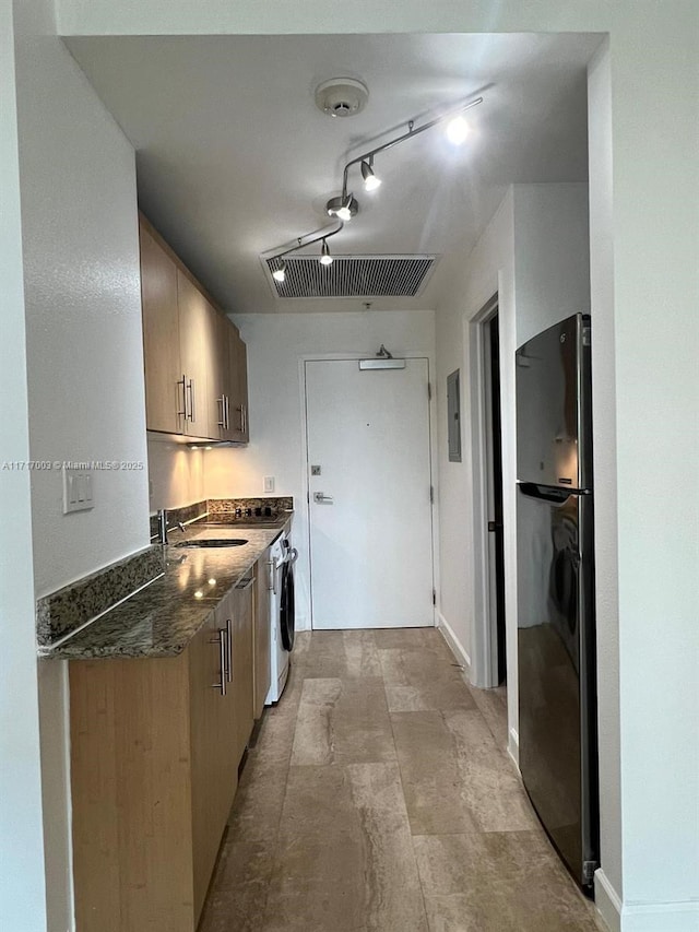 10275 Collins Ave Unit 111, Bal Harbour, FL 33154 - kitchen with rail lighting, dark stone counters, washer / dryer, sink, and black fridge