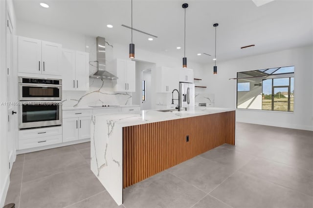 kitchen with wall chimney exhaust hood, a large island, appliances with stainless steel finishes, backsplash, and a sink