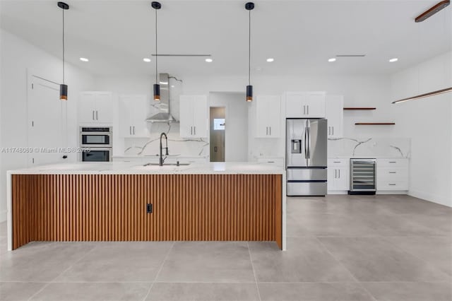 kitchen featuring tasteful backsplash, beverage cooler, wall chimney exhaust hood, stainless steel appliances, and a sink