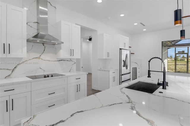 kitchen with black electric cooktop, a sink, white cabinets, wall chimney exhaust hood, and stainless steel fridge